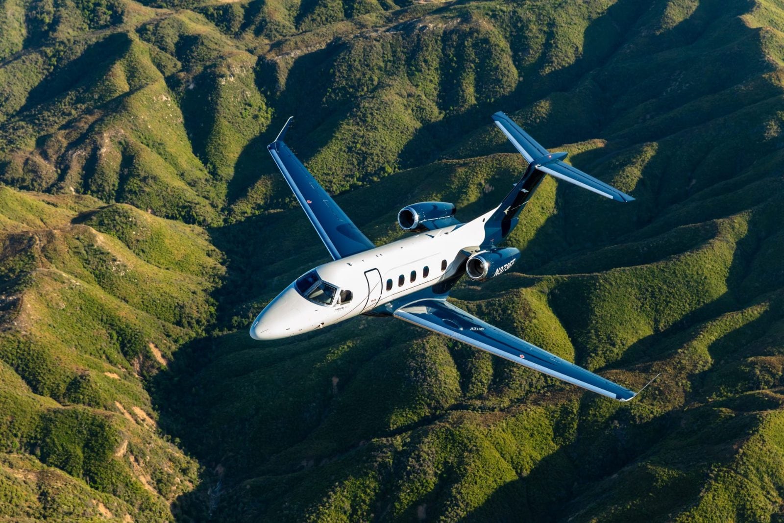 A Phenom 300E banking over green ranges — Embraer's official photography