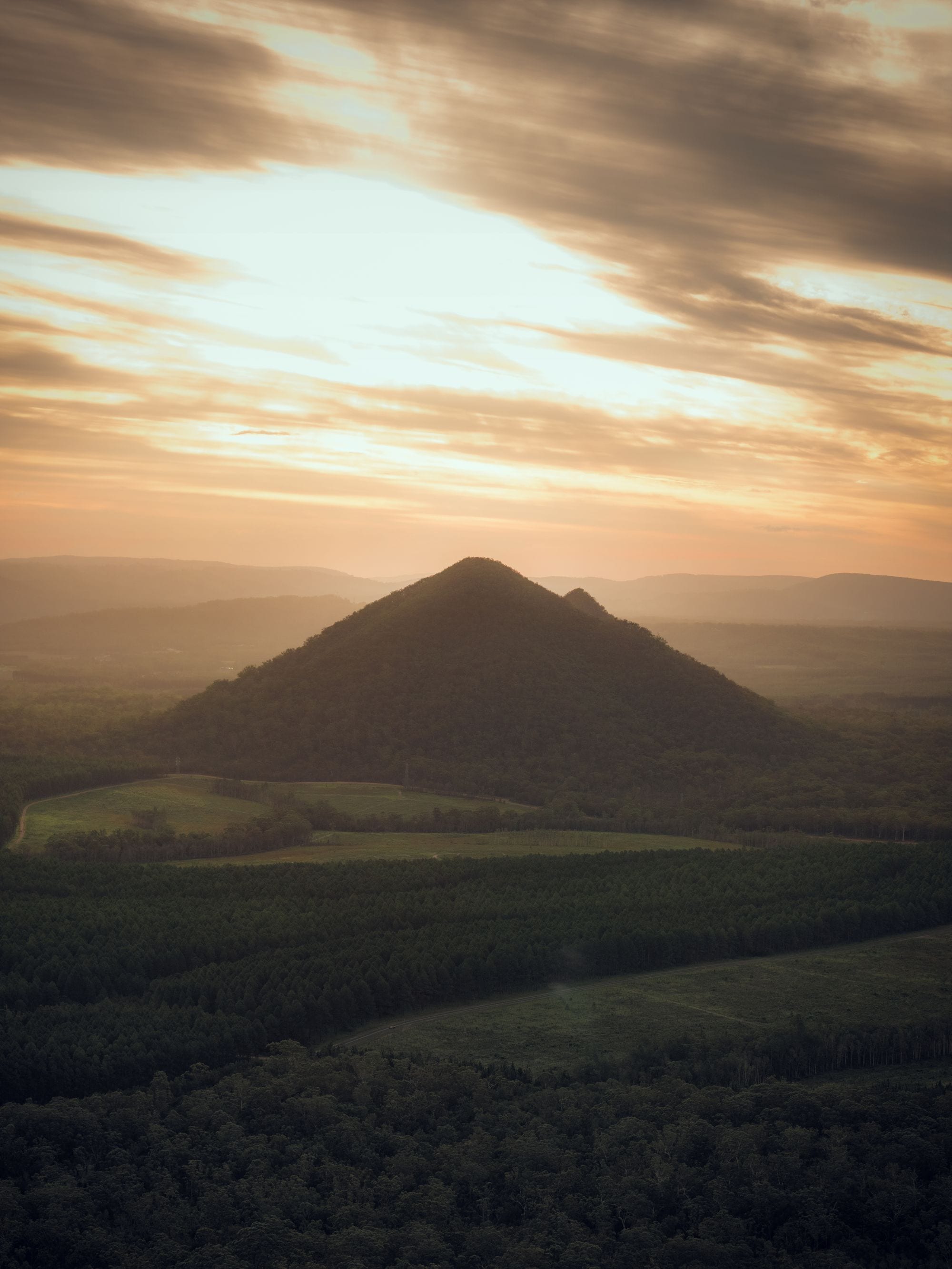 Hazy sunset over a forested peak of the Glass House Mountains in the Brisbane hinterland