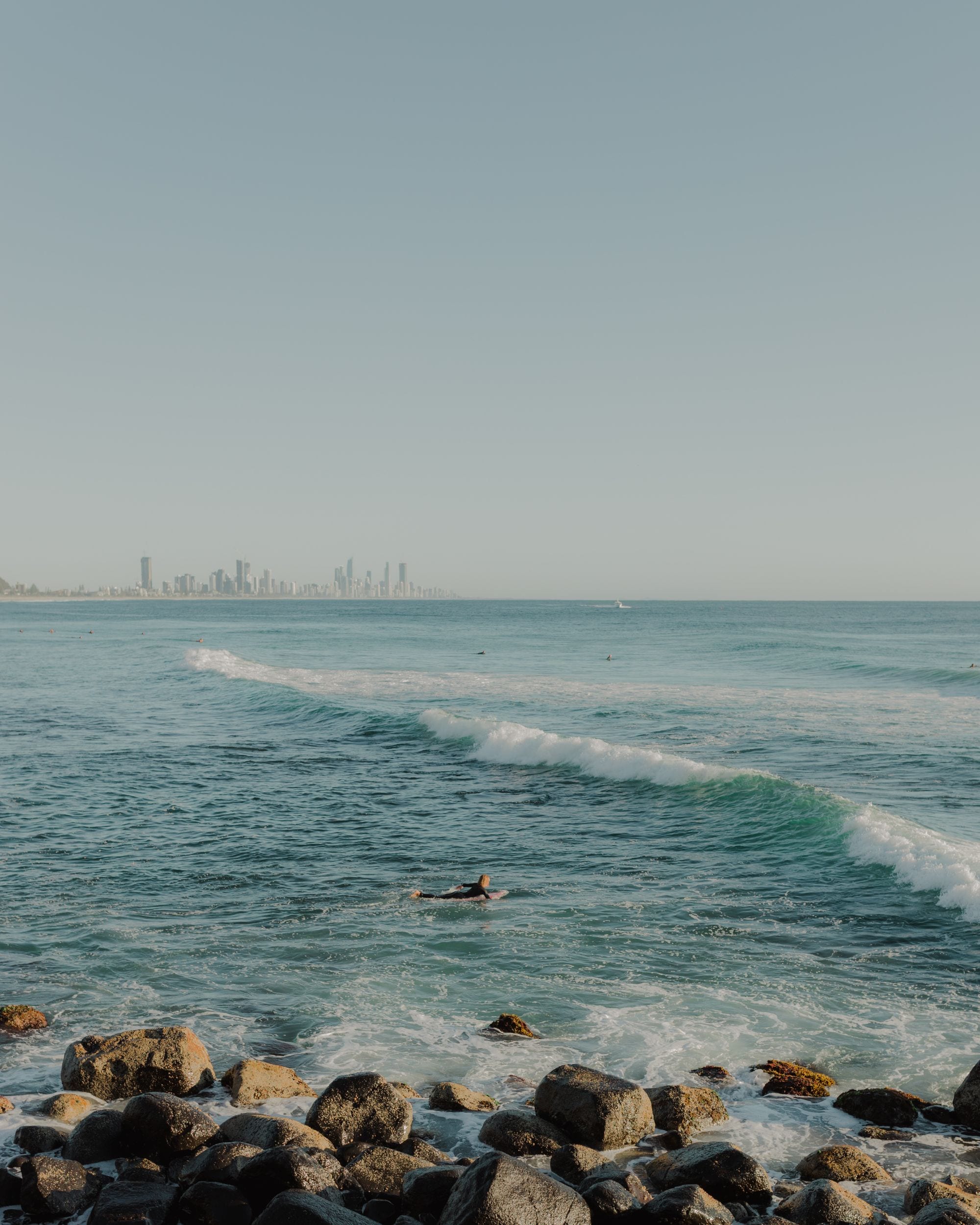 Surfer paddling out at Burleigh Heads with the Surfers Paradise skyline on the horizon