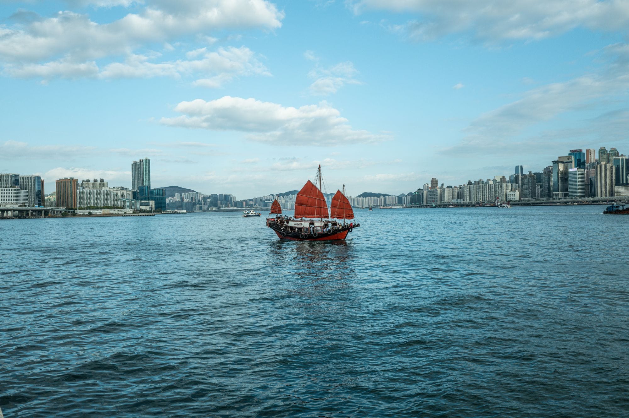 A red-sailed junk boat crossing the open waters of Victoria Harbour