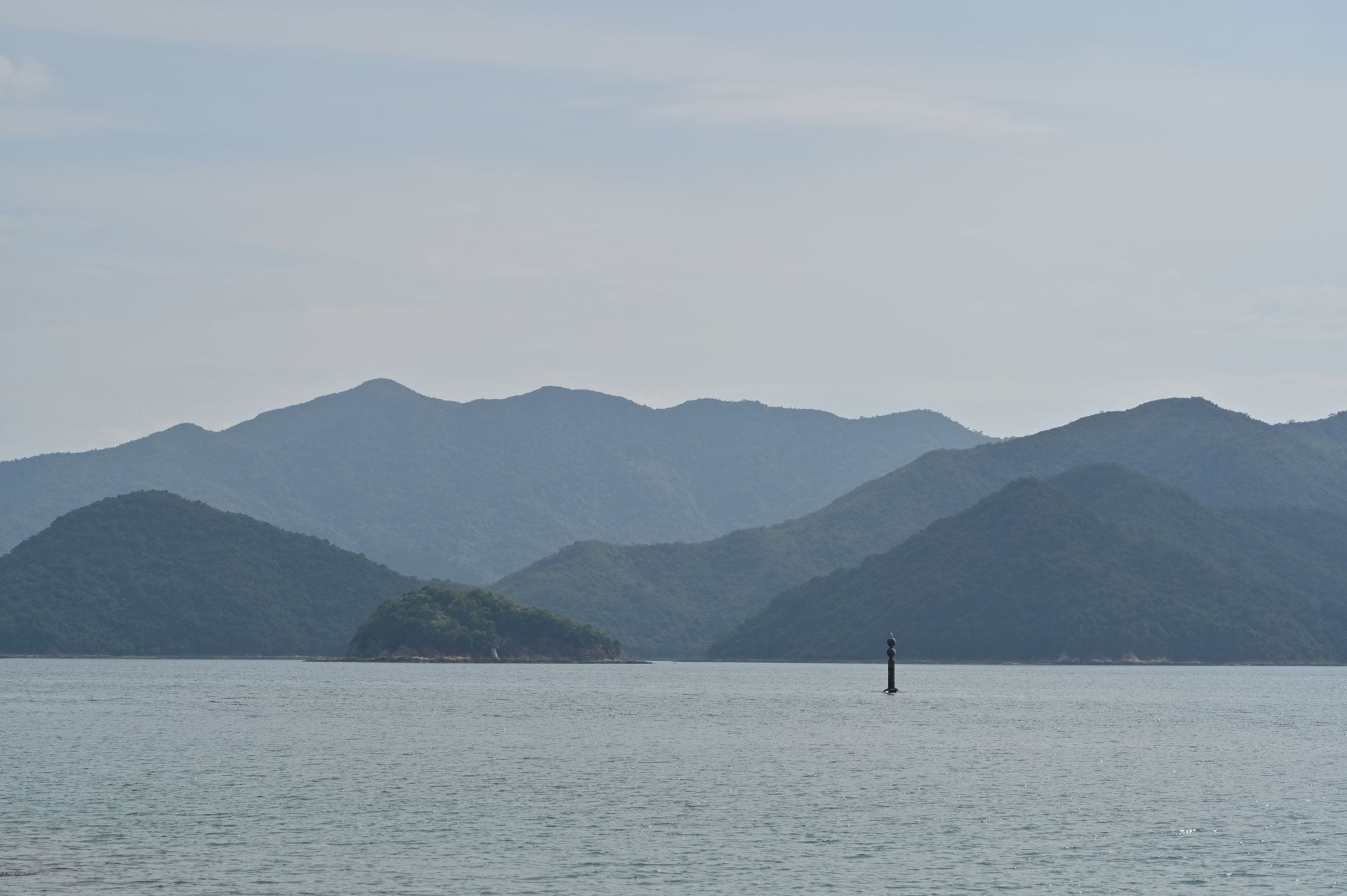 Layered green ridgelines and islands fading into soft haze over calm coastal waters east of Hong Kong
