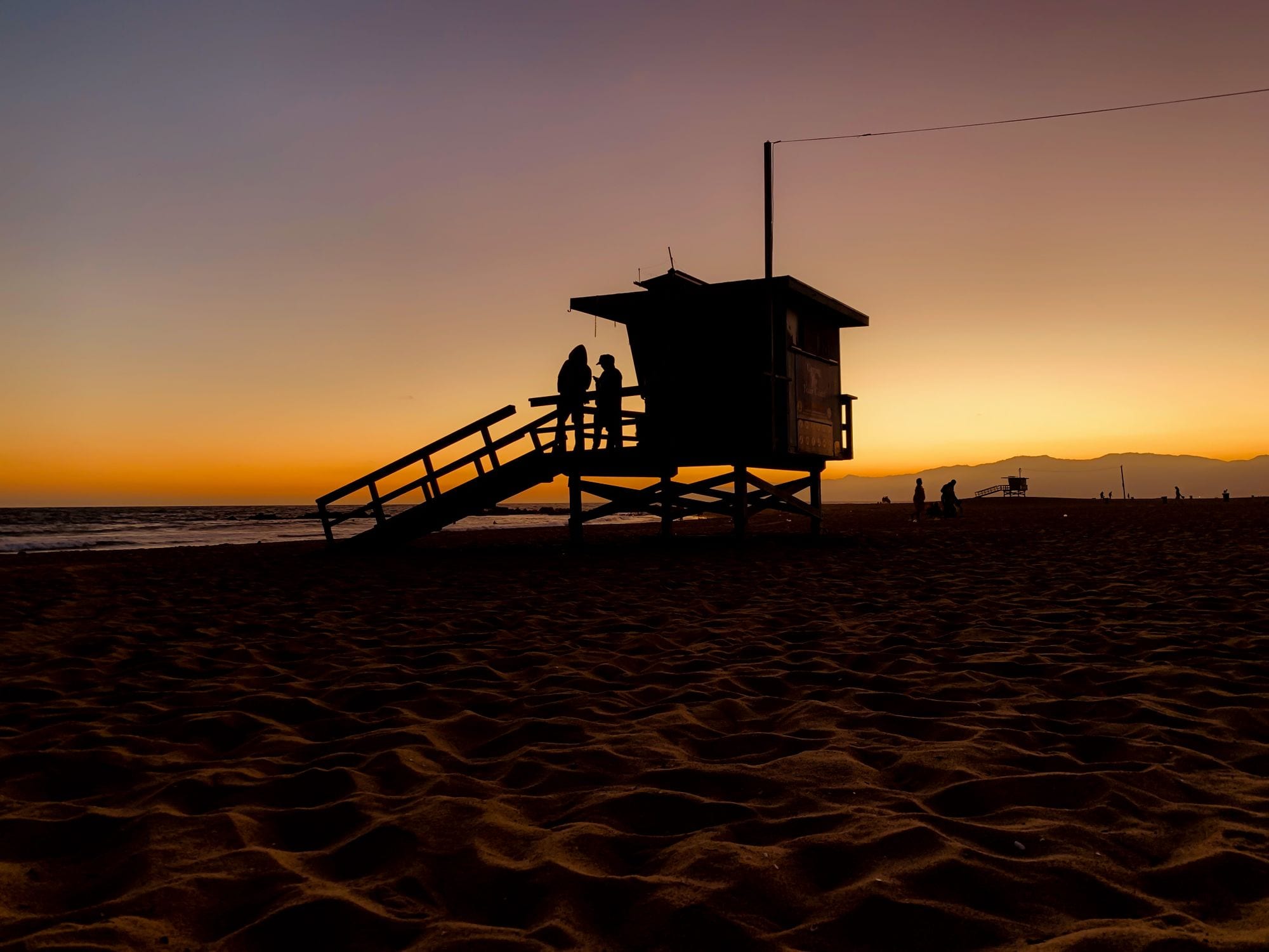 Silhouetted lifeguard tower on a quiet Los Angeles beach against a warm dusk sky
