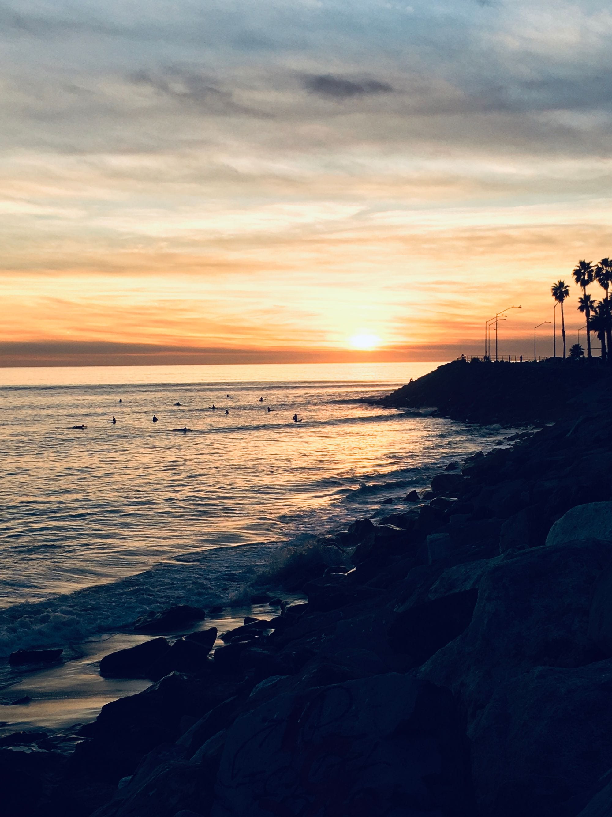 Surfers waiting in golden Pacific water at sunset off Malibu beach