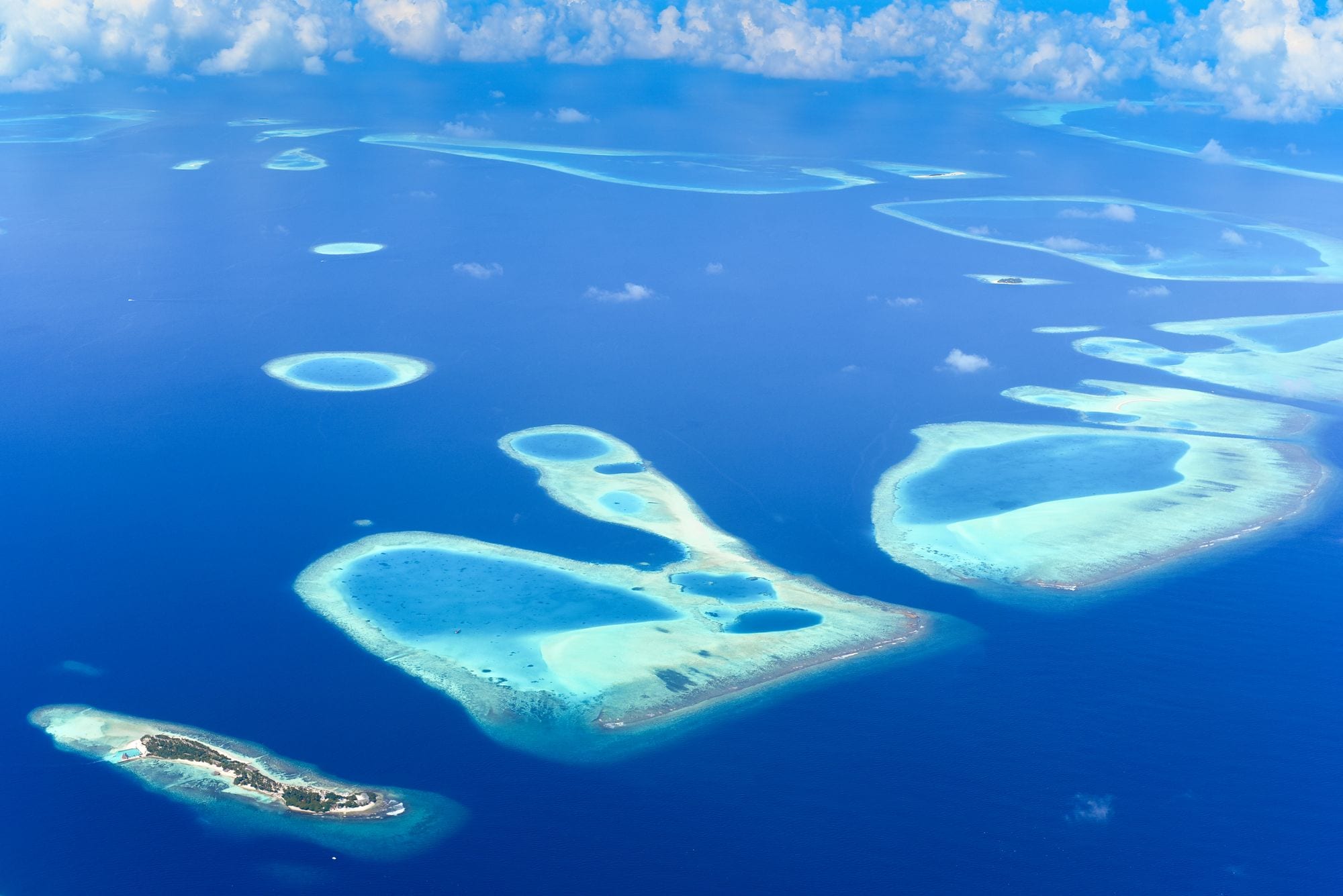 Turquoise atolls and coral rings scattered across the deep blue Indian Ocean from above