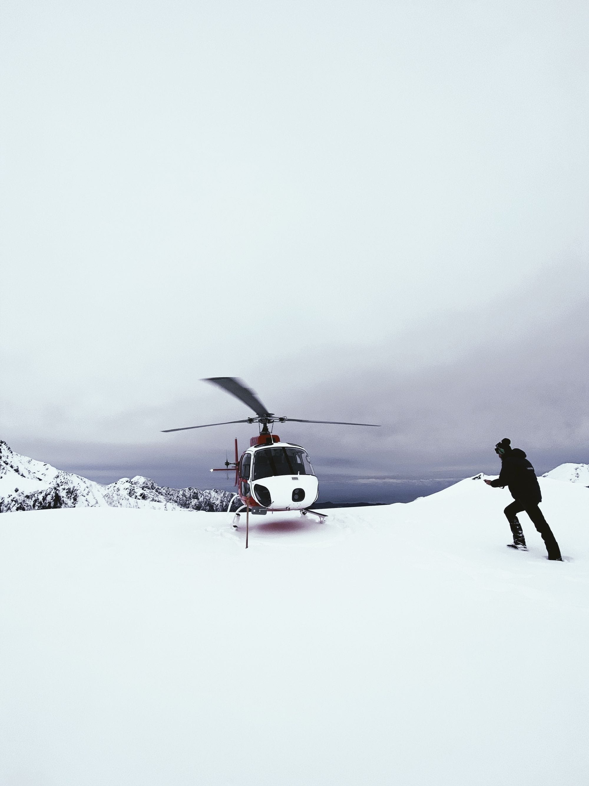 A lone skier walks toward a waiting helicopter on a remote alpine snowfield