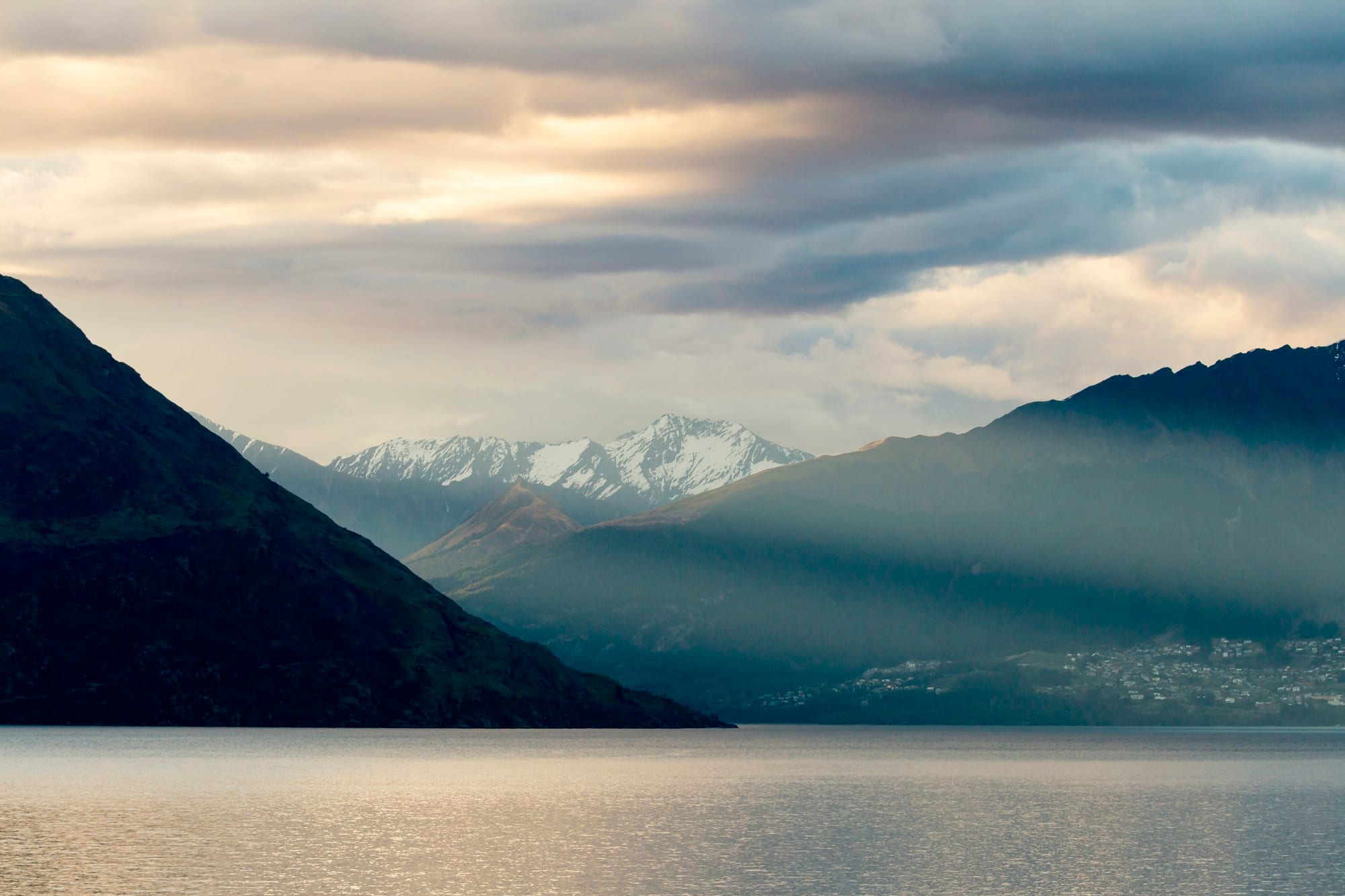 Evening light breaking over snow-capped peaks above the still waters of Lake Wakatipu