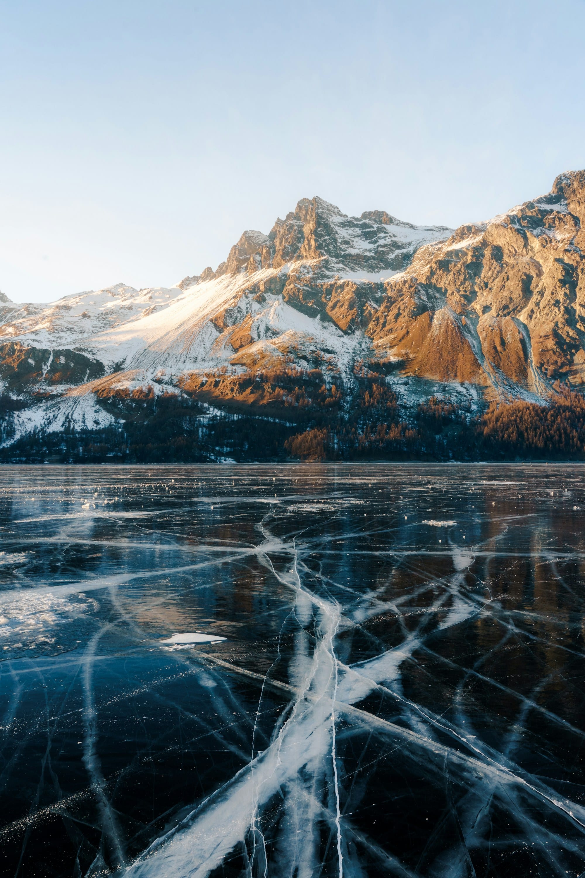 Golden alpenglow on Engadin peaks above the cracked ice of frozen Lake Sils