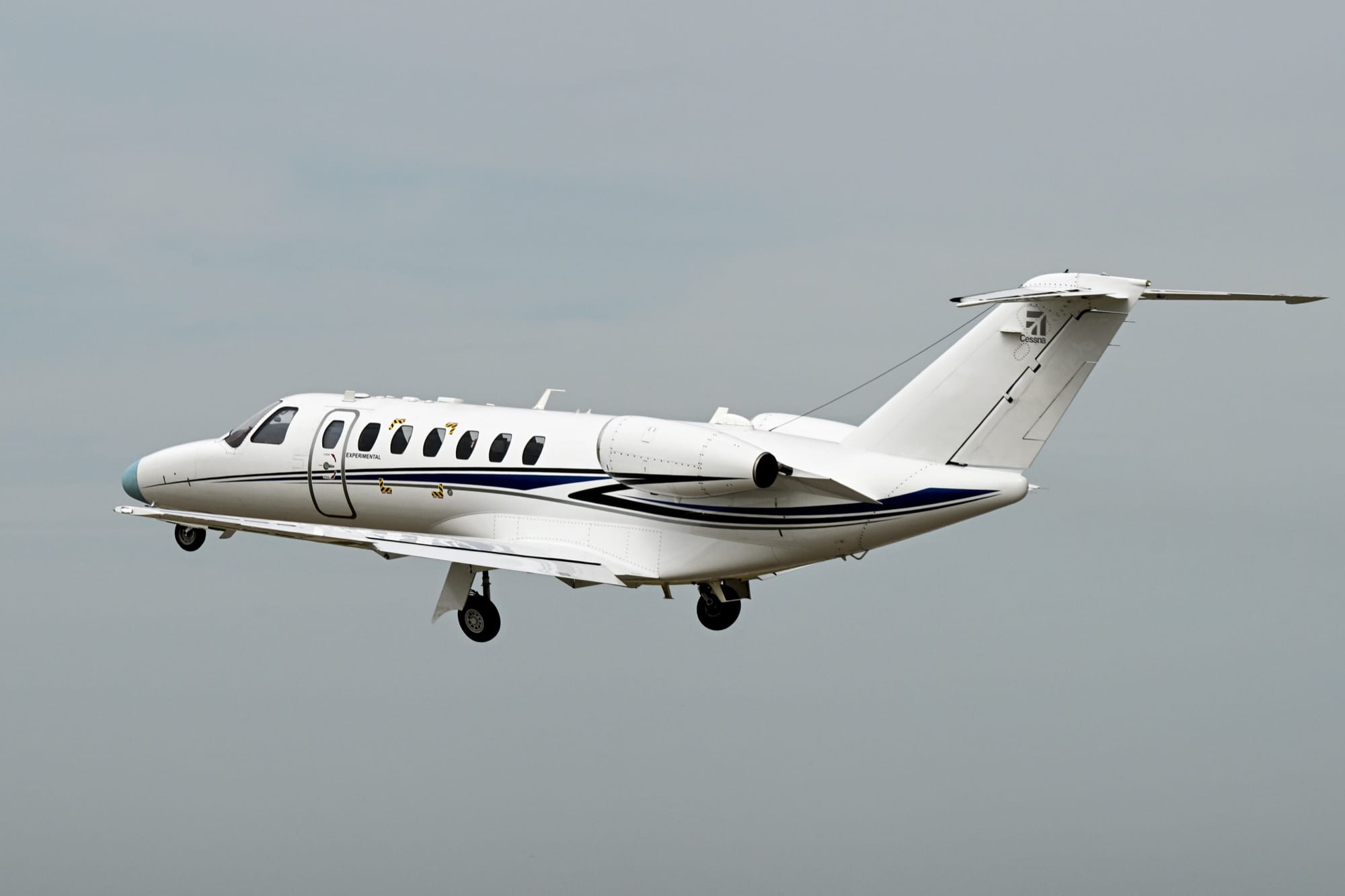 The Citation CJ3 Gen3 prototype climbing gear-down against a grey sky, test boom fitted