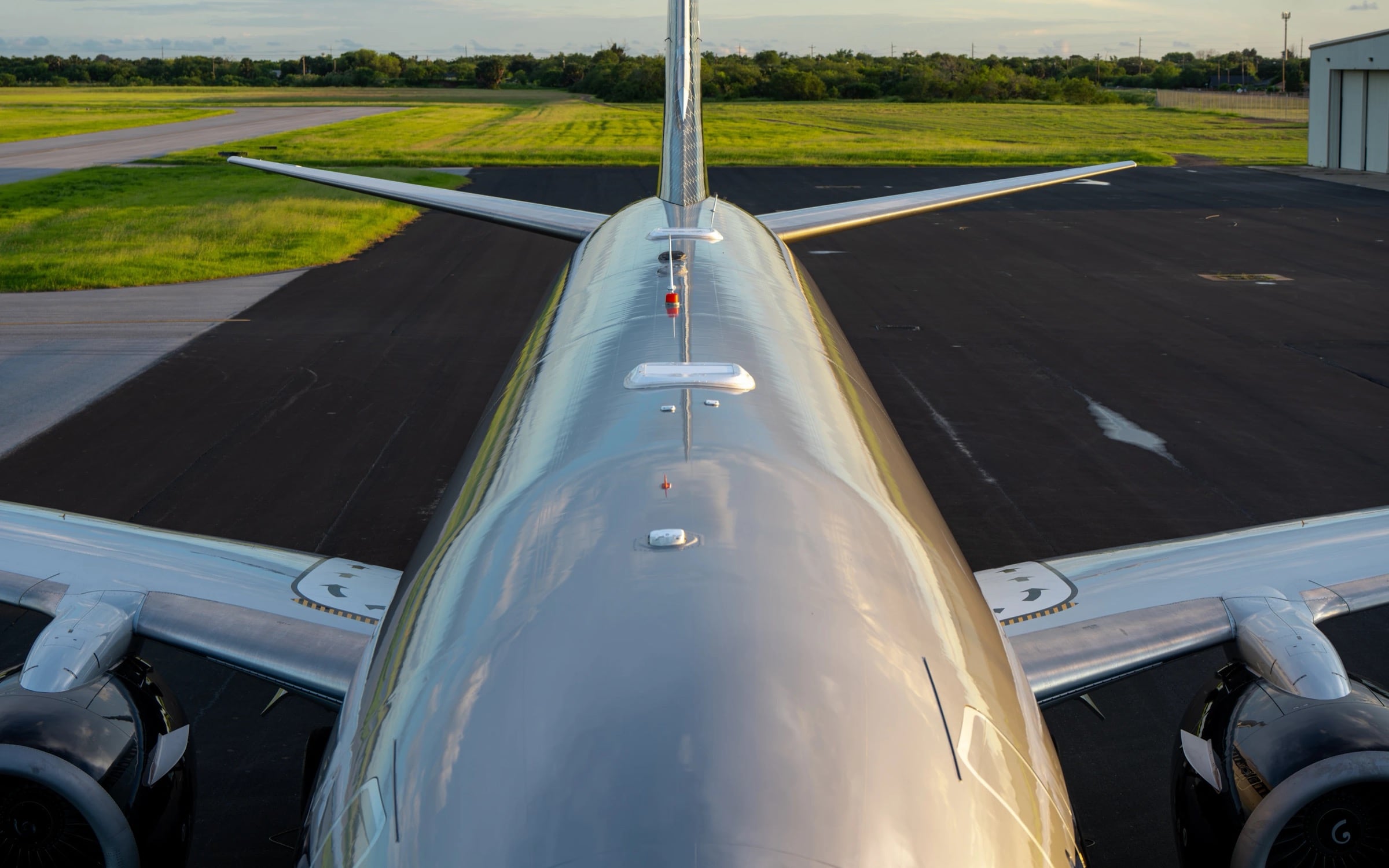 Looking forward along the polished crown of a business jet at golden hour, low-profile satellite antenna fairings on the fuselage spine