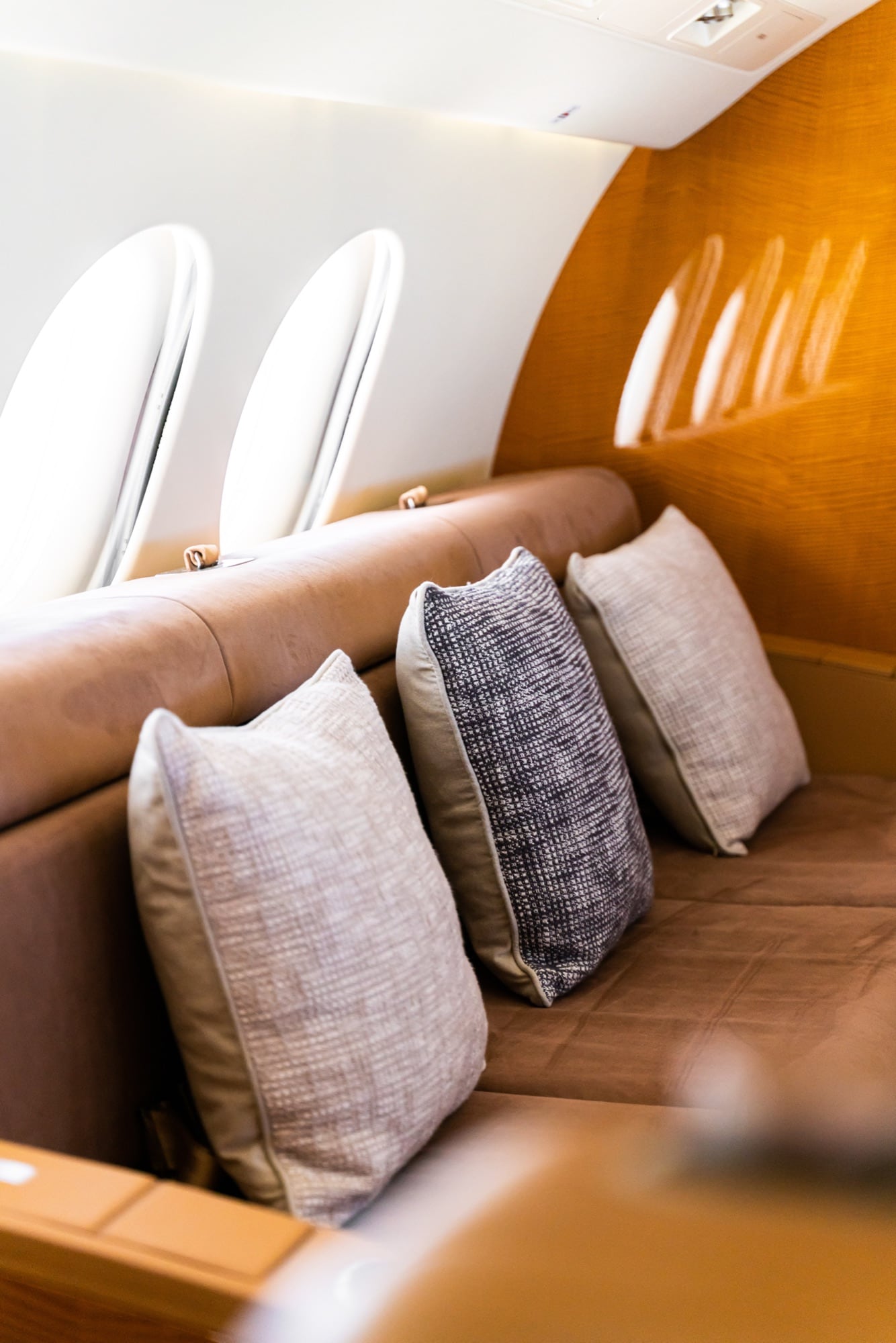 The Falcon 7X aft lounge — a divan dressed in pale fabric beneath the cabin's quiet light