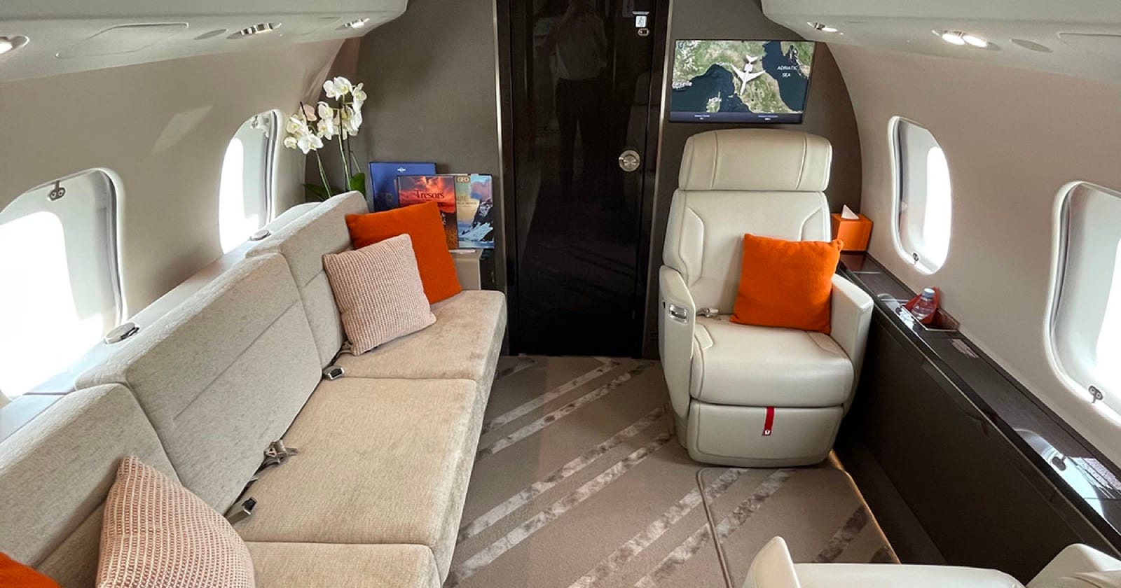 The aft lounge of a Global 6500 — cream divan and club seat with orange cushions, flight map on the bulkhead screen